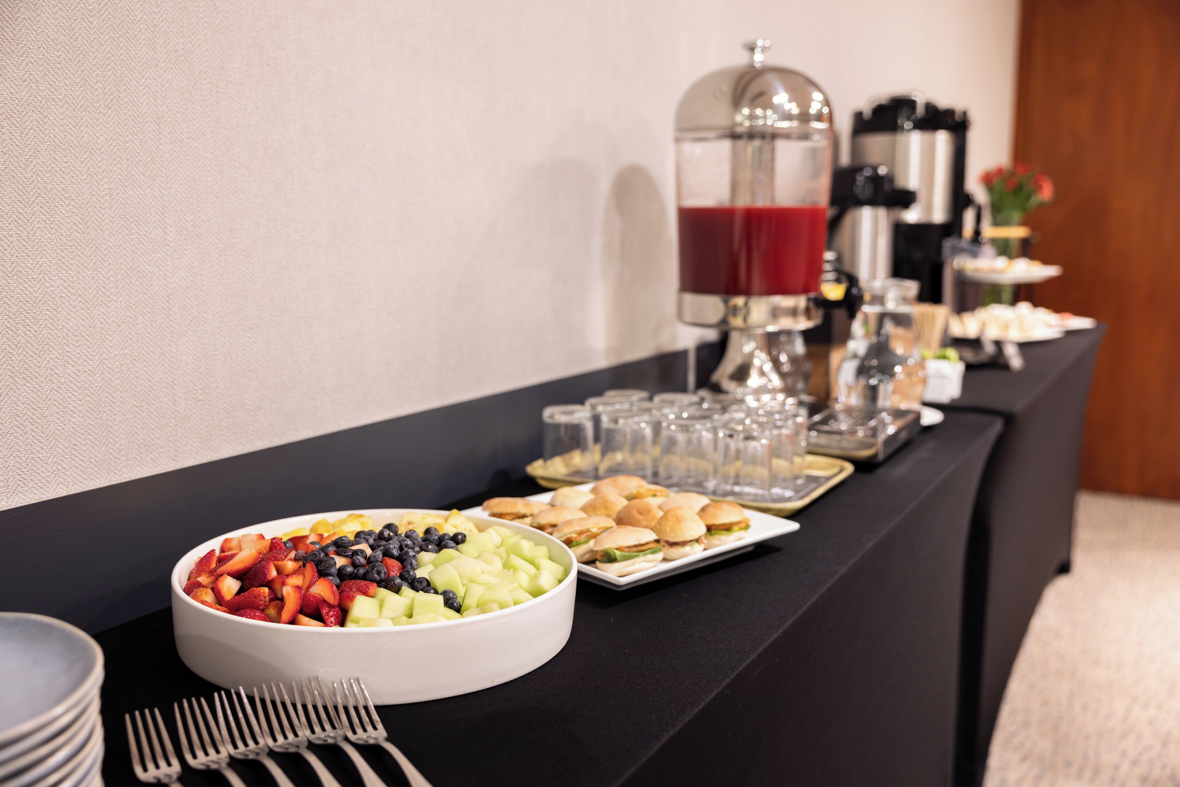 A buffet table with various food items, including a bowl of fruit and sandwiches, and a coffee station with a coffee maker and cups.