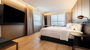 Ein modernes Hotelzimmer mit einem großen Bett, einem flachbildfernseher an der Wand und einem Schreibtisch mit einer Lampe.