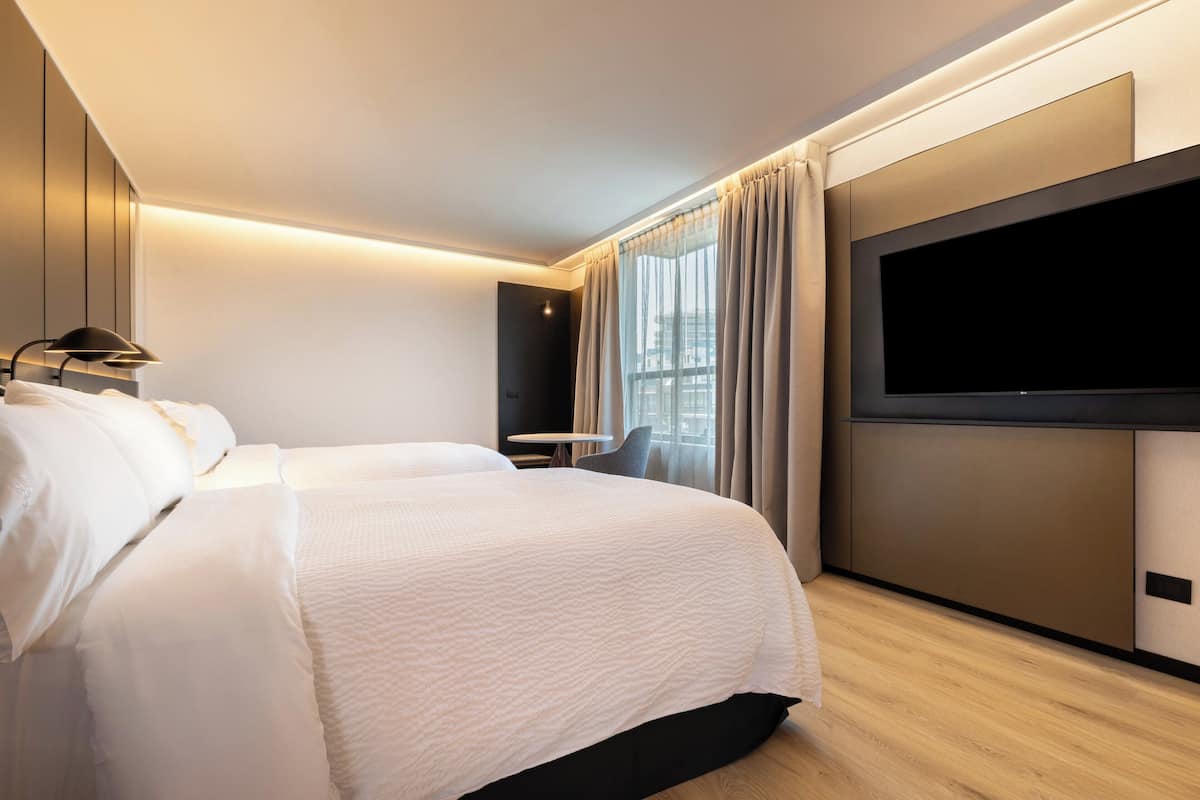 Una habitación de hotel moderna con una cama grande, un televisor de pantalla plana, una mesita pequeña y una silla.
