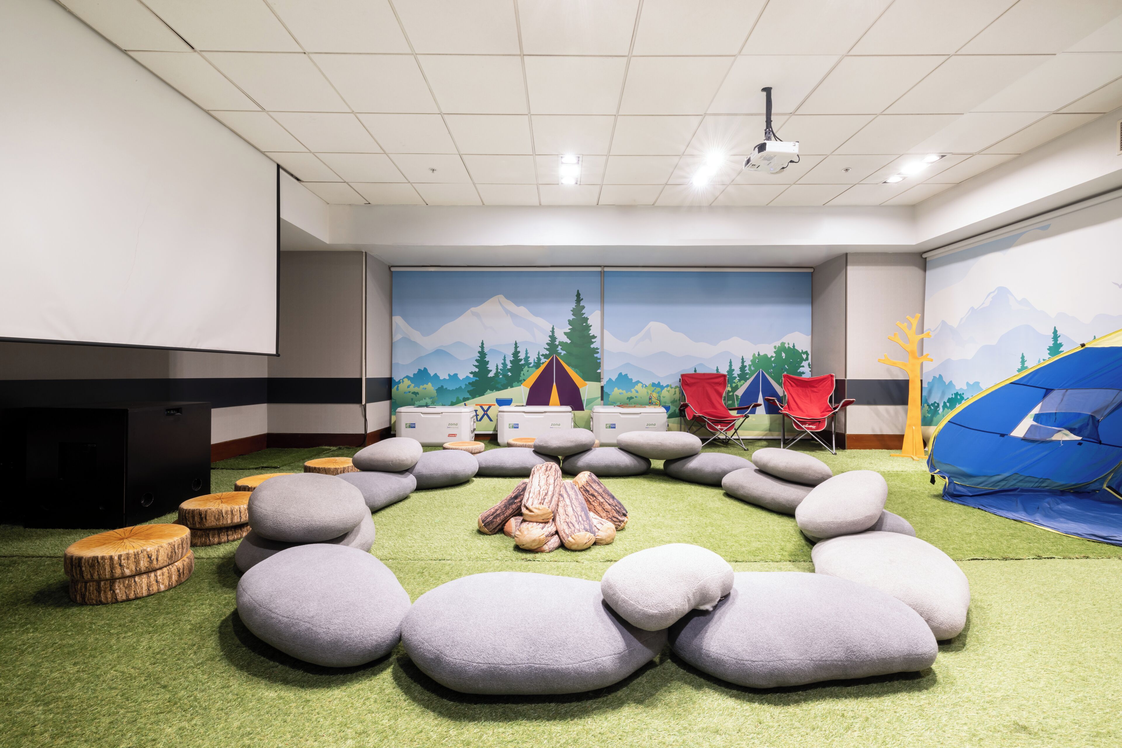 A room with a circular seating arrangement of large cushions, a tent, and a projector screen on the wall.