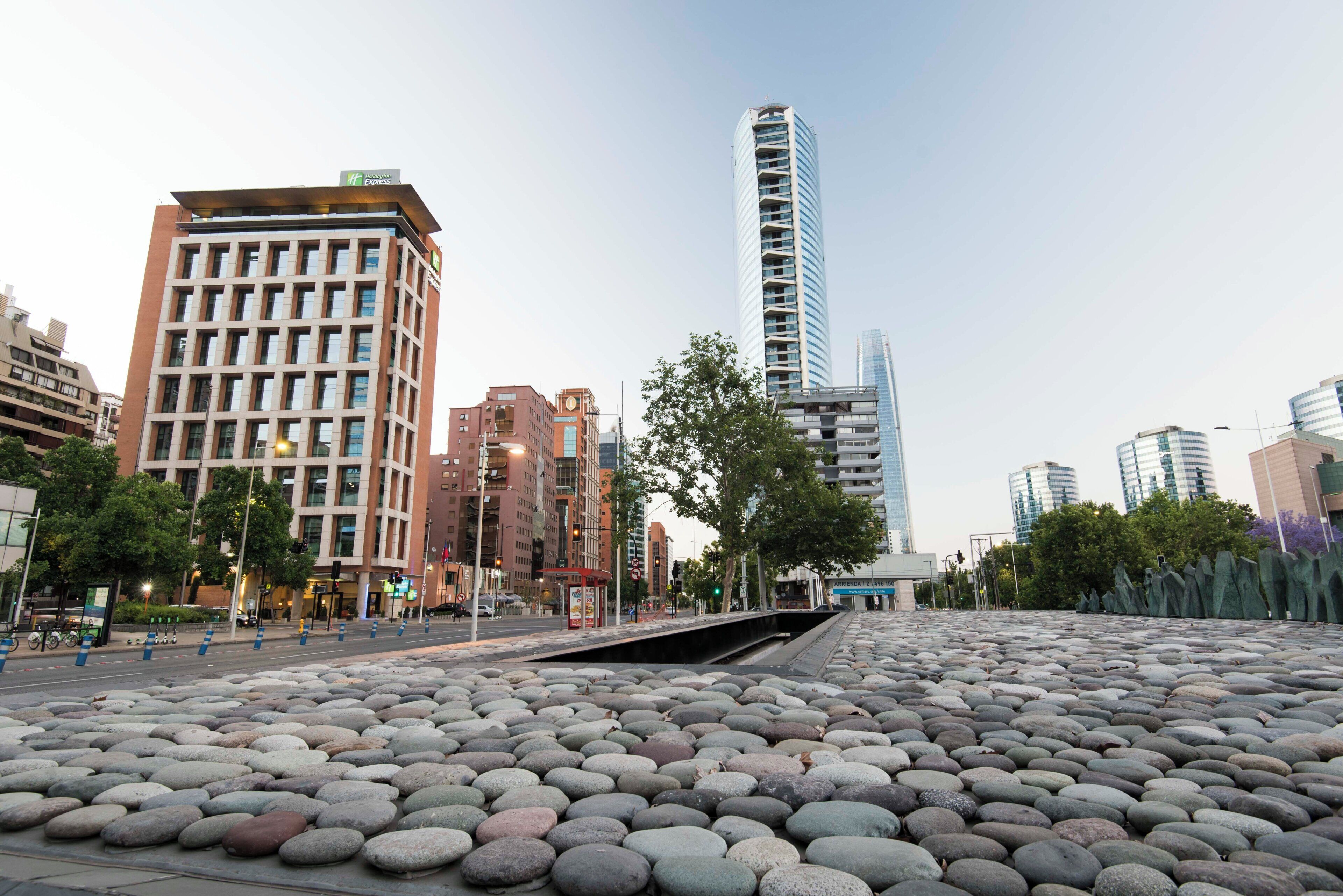 Un paisaje urbano con edificios modernos, un hotel con letrero visible y una zona pavimentada con piedras.