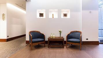 A reception area with two wooden chairs, a small table with vases, and three wall-mounted light fixtures.