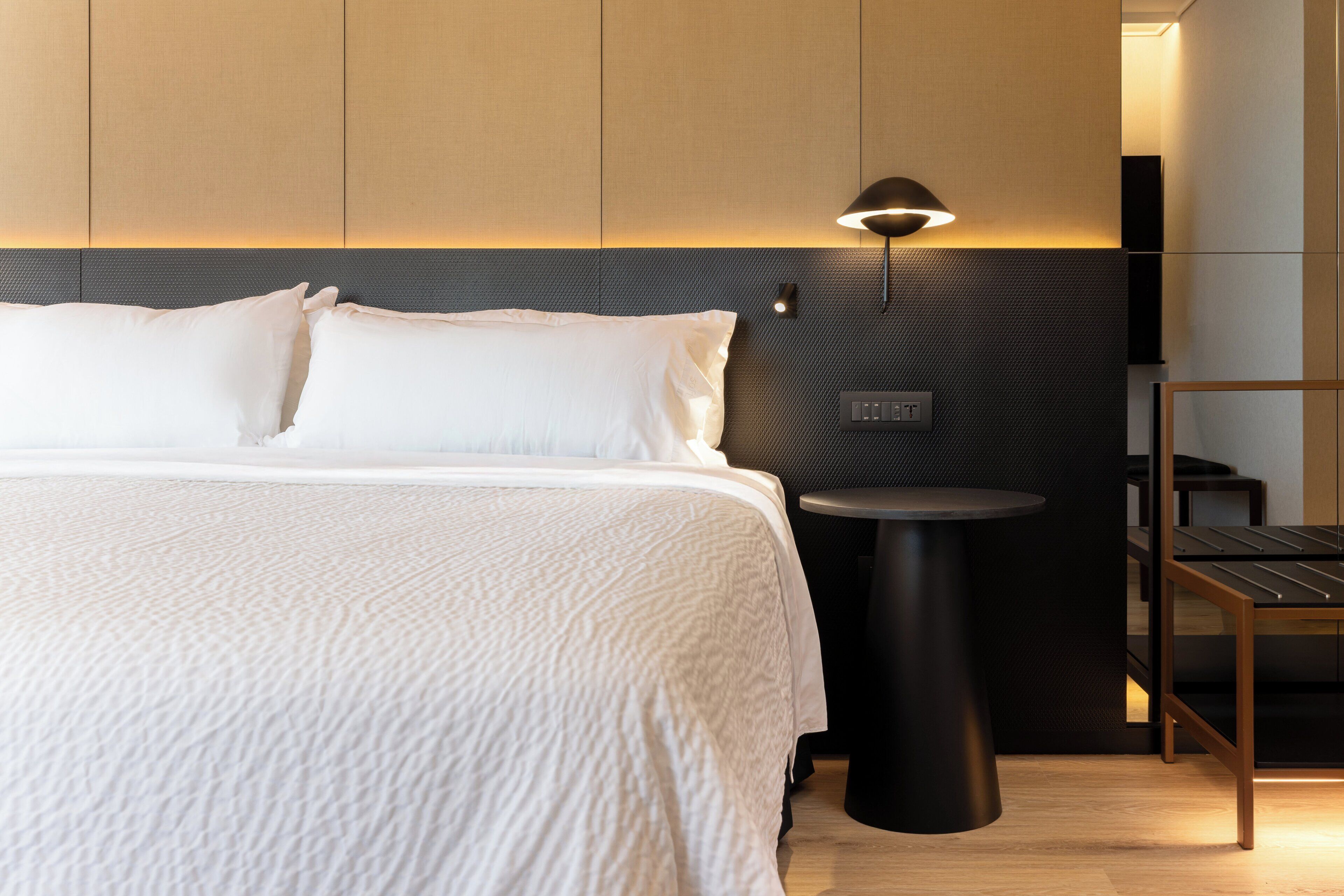 Una habitación de hotel moderna con una cama grande, una mesita redonda y una lámpara de pared.