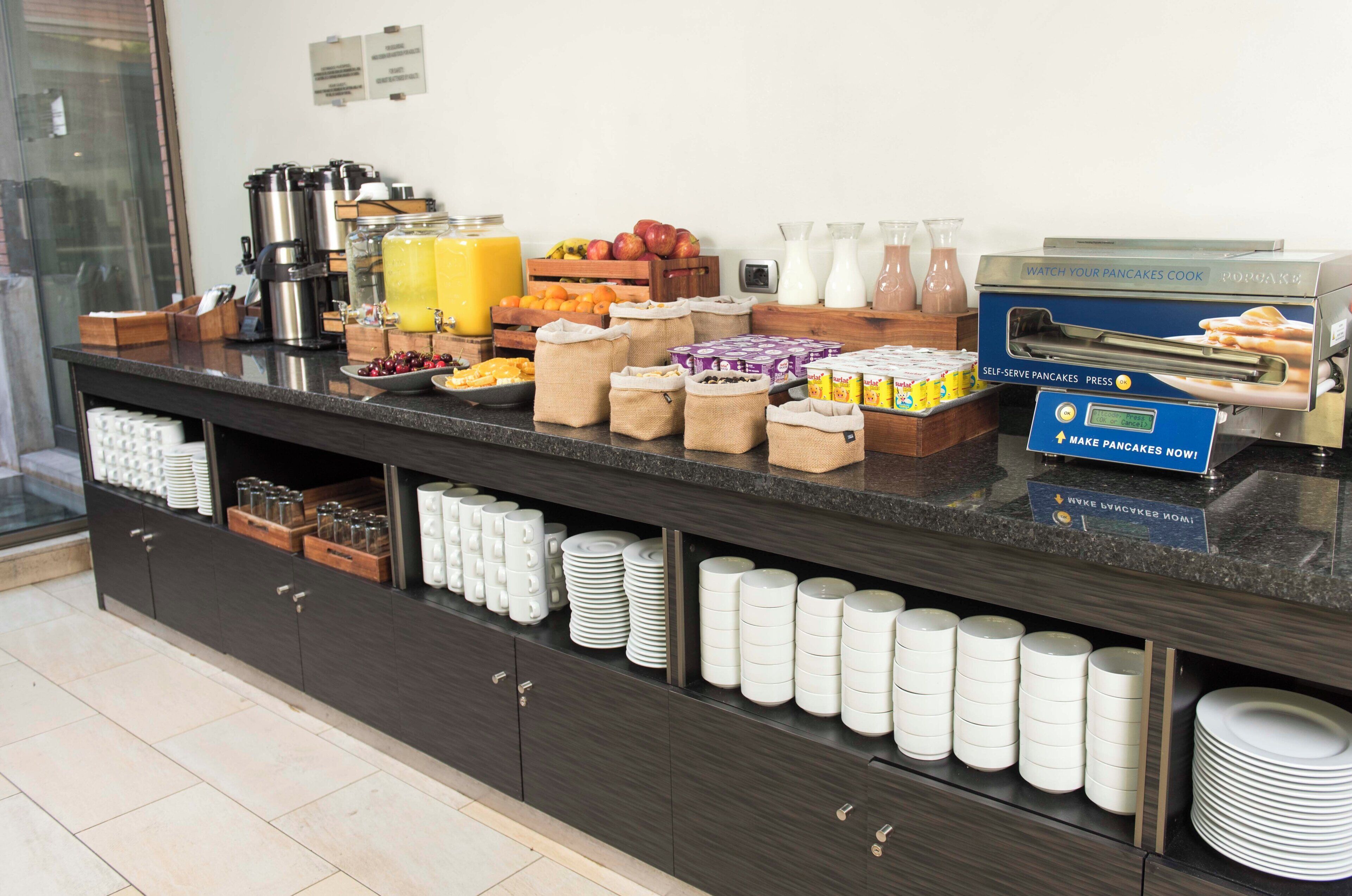 Buffet d'esmorzars amb diferents plats, una màquina per fer crepes i plats i gots disposats amb cura.