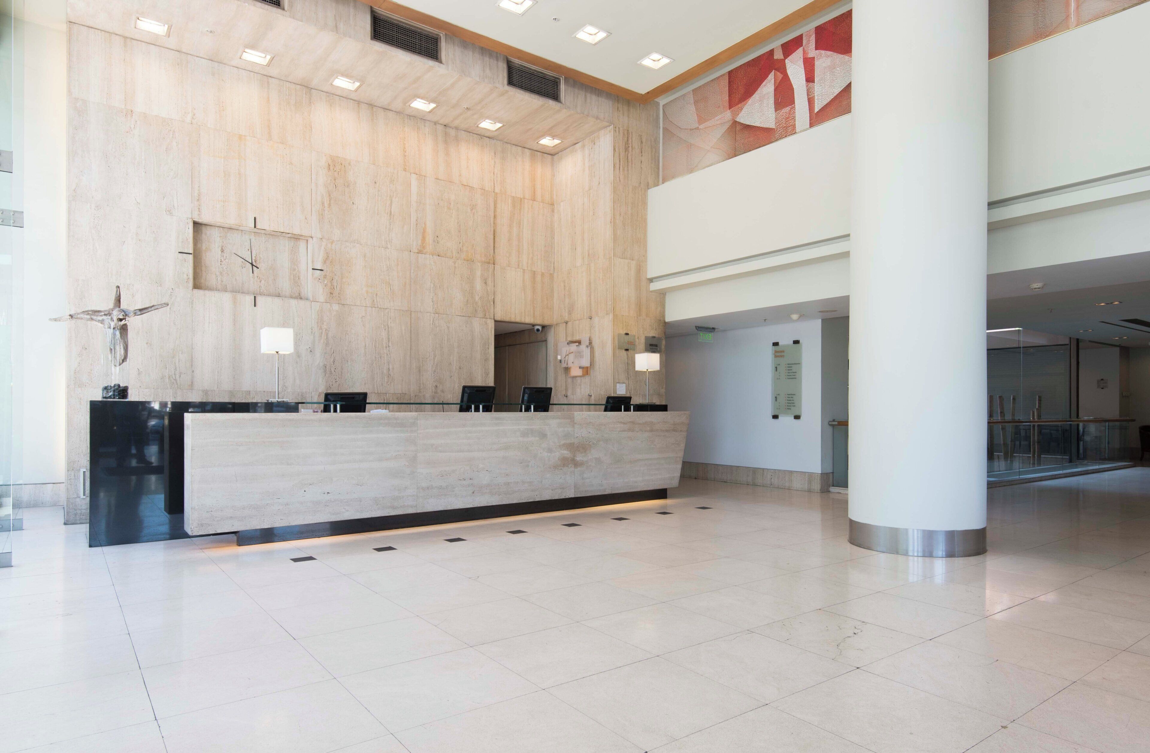 A spacious lobby with a reception desk, a large wall clock, and a high ceiling with recessed lighting.