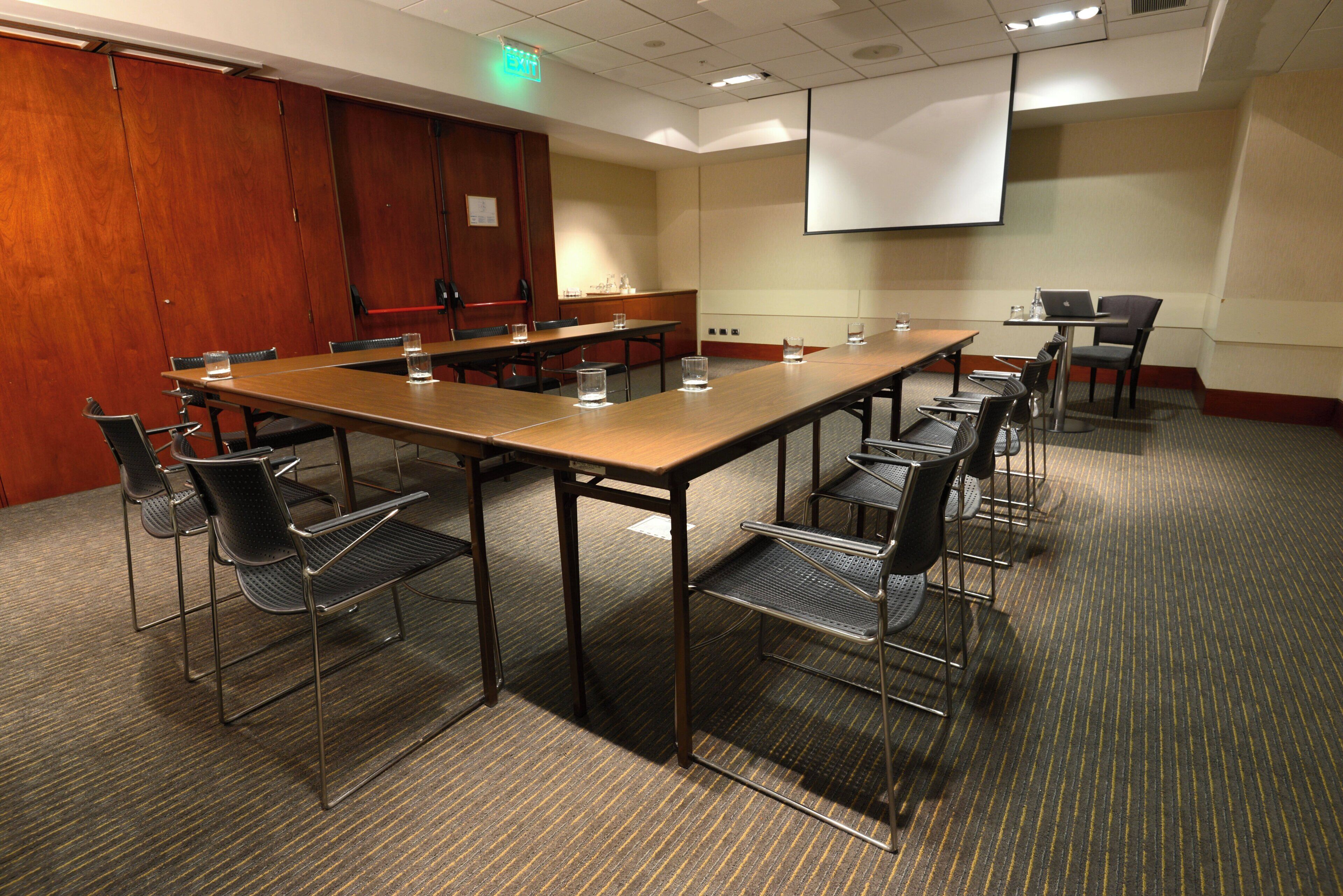 A conference room with a long table, chairs, a projector screen, and a water dispenser.