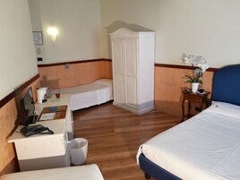 A hotel room with a bed, a desk with a telephone, a small table with a plant, and a wardrobe.