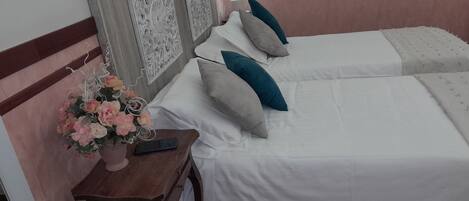 Une chambre d’hôtel avec deux lits, une table de chevet en bois ornée d’un vase de fleurs et un mur décoré de panneaux.
