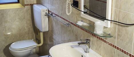 Een badkamer met toilet, bidet en wastafel, een spiegel en een lamp.