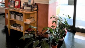 A reception area with a wooden desk displaying books and brochures, a wall-mounted lamp, and potted plants. - Hotel San Felice (Bologna)