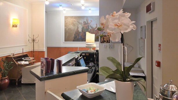 A reception area with a counter, a painting on the wall, and a potted orchid. - Hotel San Felice (Bologna)