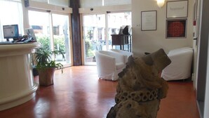 A reception area with a stone sculpture, a reception desk, a potted plant, and a seating area with white chairs. - Hotel San Giorgio (Bologna)
