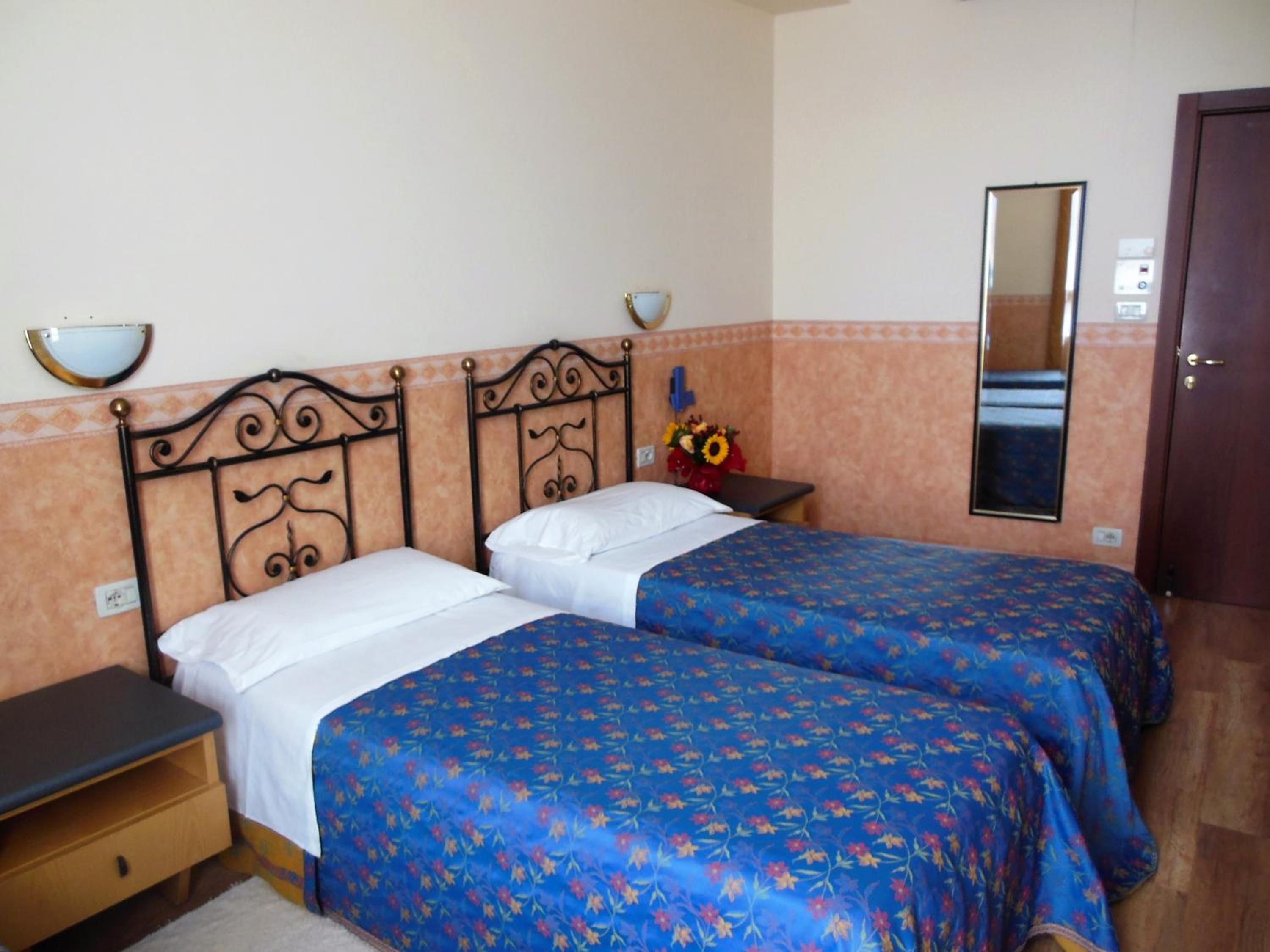 A hotel room with two beds, a nightstand, a mirror, and a door.