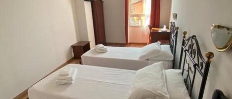 Ein Zimmer mit zwei Betten, einem Deckenventilator, einem Fernseher und einem Fenster mit Vorhängen.