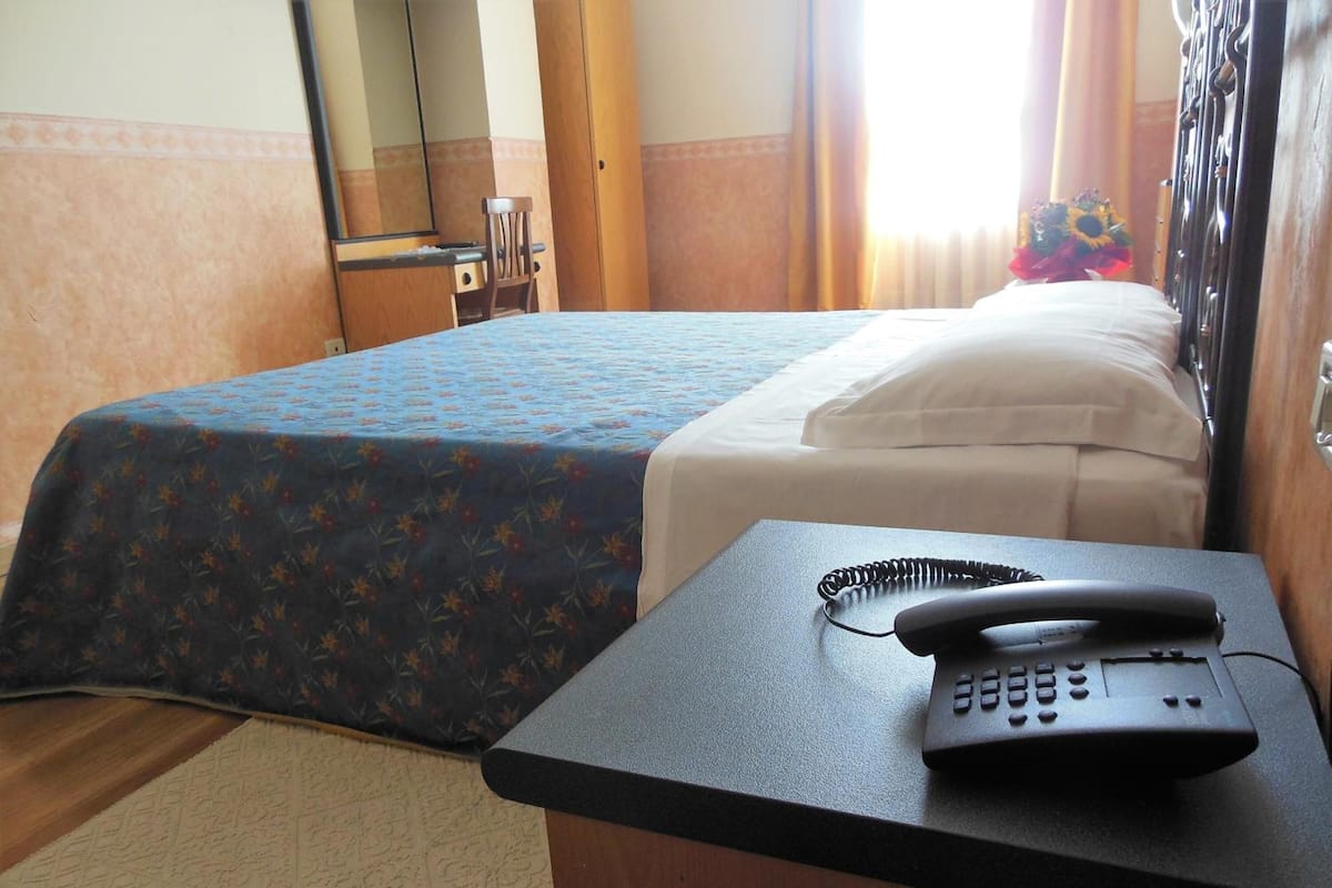 Ein Hotelzimmer mit einem Bett, einem Schreibtisch mit Telefon, einem Sessel und einem Spiegel.