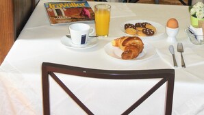 A breakfast setup with a table, chairs, a book, a glass of orange juice, and pastries. - Hotel San Giorgio (Bologna)
