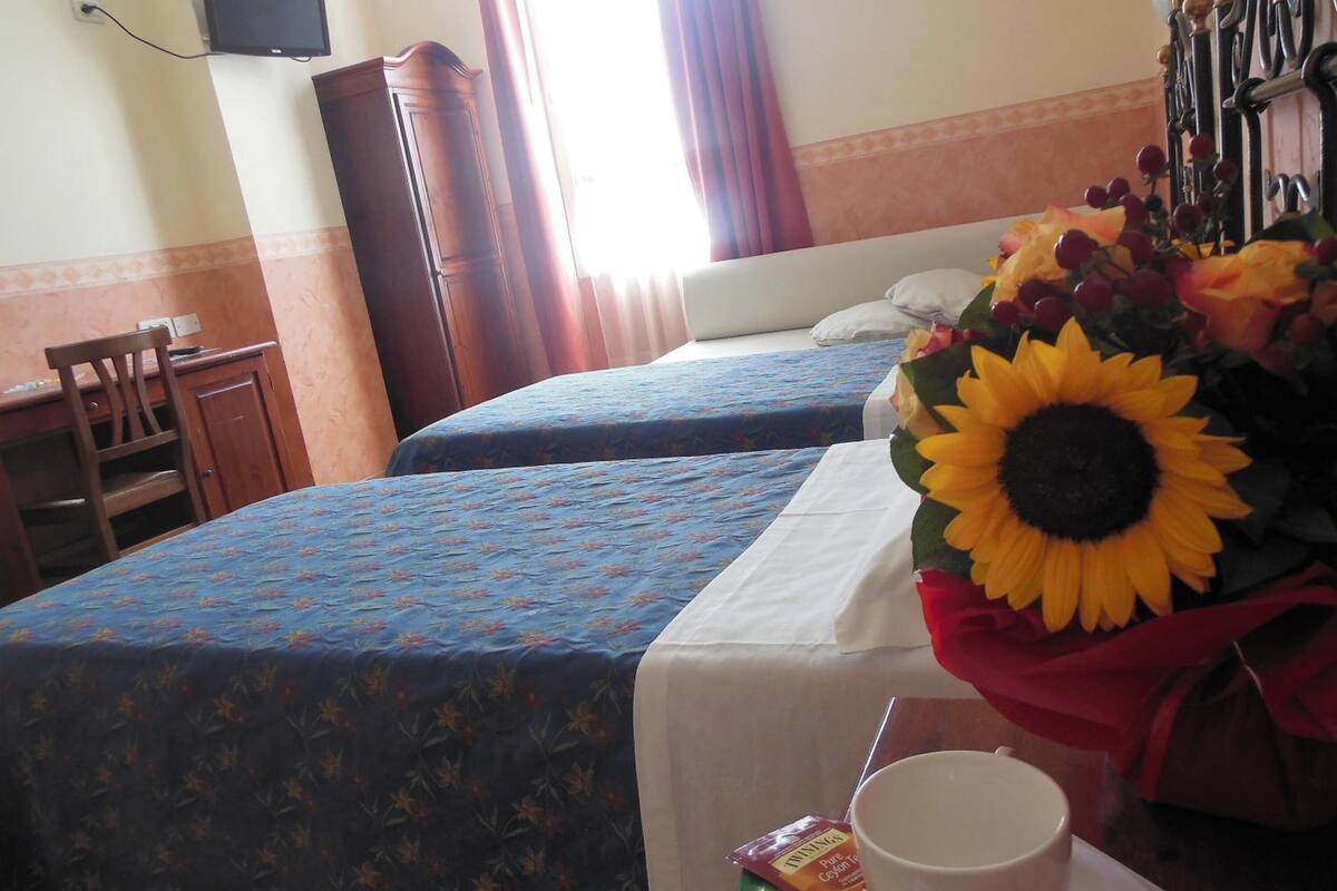 Ein Hotelzimmer mit zwei Betten, einem Schreibtisch, einem Fernseher und einem Blumenstrauß.