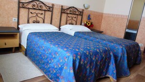 A double bed with a floral bedspread, a nightstand, a mirror, and a small table with a vase of flowers. - Hotel San Giorgio (Bologna)
