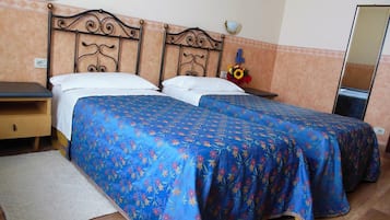 Una cama doble con colcha estampada, una mesita de noche, un espejo y una pequeña mesa con un florero.