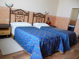 Una cama doble con colcha estampada, una mesita de noche, un espejo y una pequeña mesa con un florero.