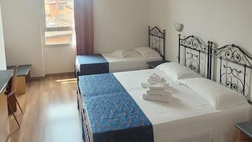 Habitación de hotel con dos camas, un escritorio y vistas a edificios.
