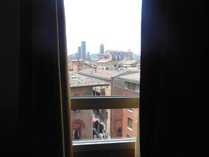 A view through a window of a cityscape with buildings and a prominent tower. - Hotel San Giorgio (Bologna)