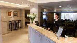 A hotel reception area with a marble counter, two framed artworks on the wall, and a vase with white flowers. - Argentino Hotel (Mendoza)