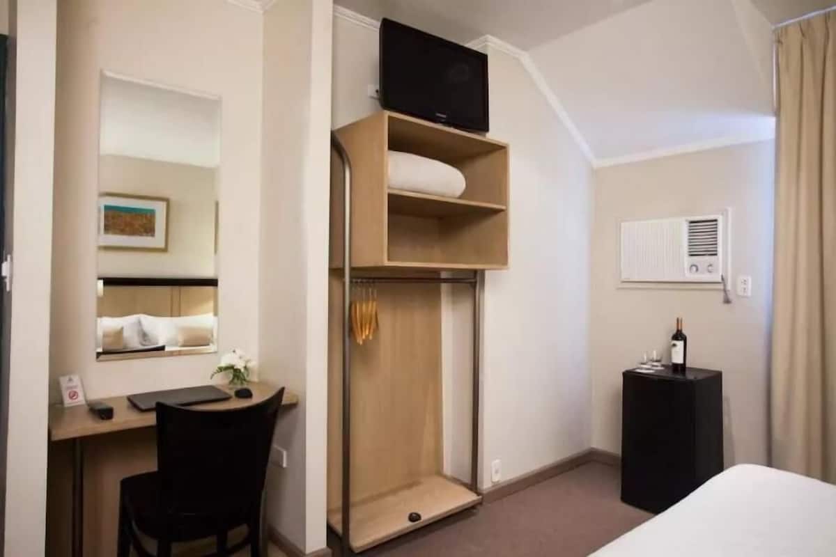 A hotel room with a desk, chair, wardrobe, and a bed.
