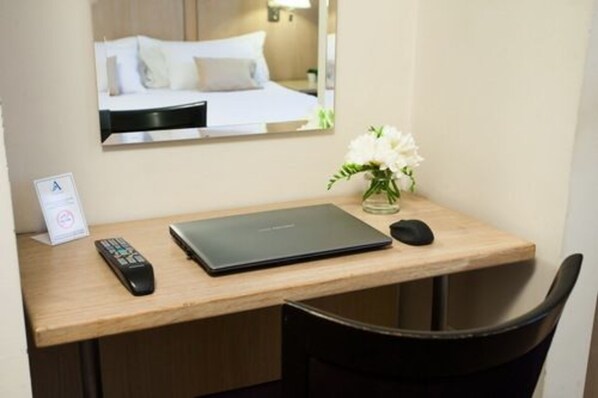 A hotel room desk with a laptop, a remote control, a mouse, and a vase with flowers. - Argentino Hotel (Mendoza)