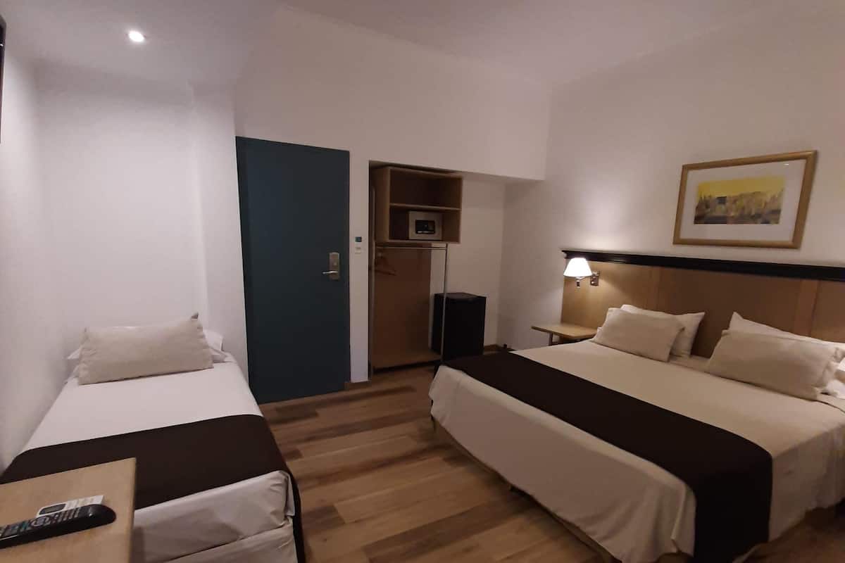 A hotel room with two beds, a desk, a chair, a TV, a microwave, and a painting on the wall.