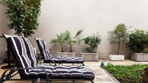 A patio area with two lounge chairs and a small table, surrounded by potted plants and a stone wall. - Argentino Hotel (Mendoza)