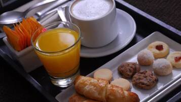 Una bandeja de desayuno con jugo de naranja, una taza de café y diversos pasteles.