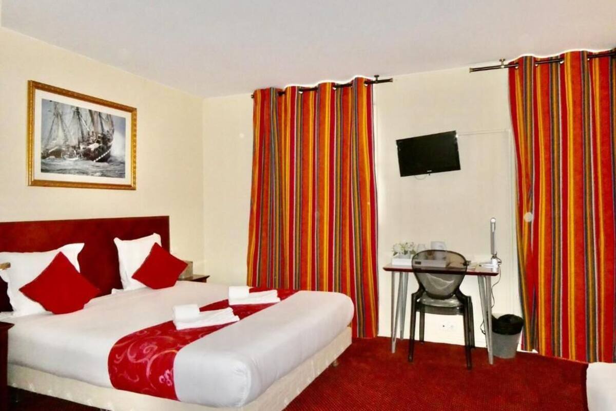 Een hotelkamer met een bed, een bureau, een stoel, een televisie en gordijnen.