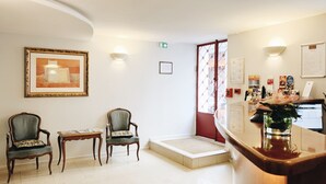 Een receptiegedeelte met twee fauteuils, een bijzettafeltje, een receptiebalie en een deur naar buiten.