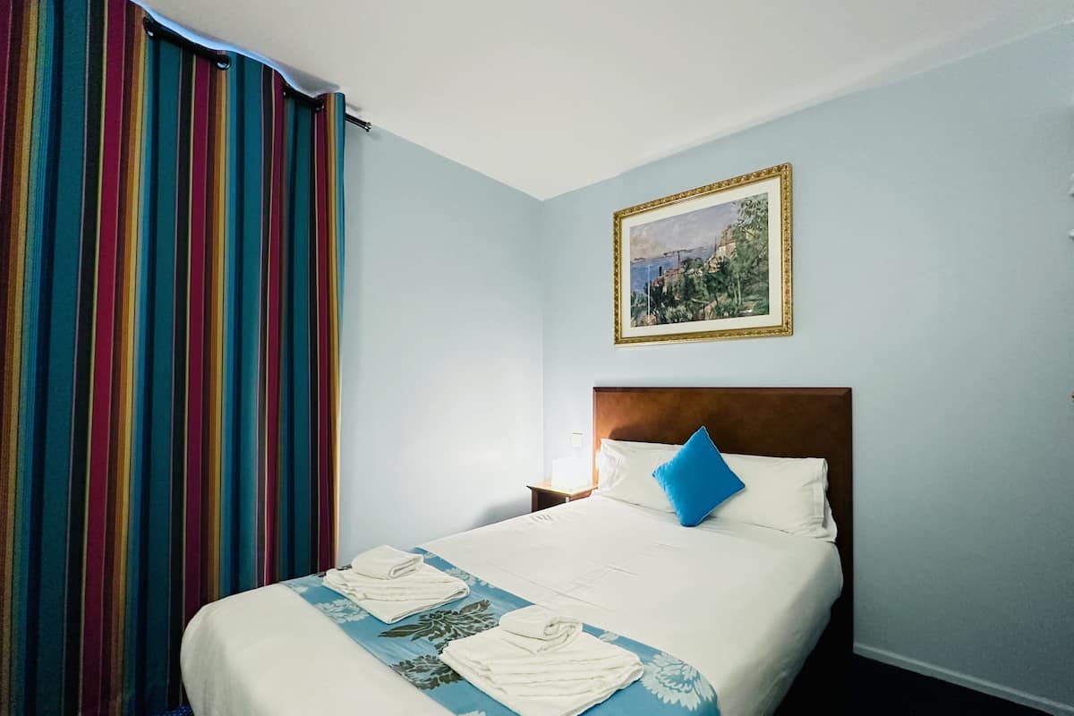Een hotelkamer met een bed, een schilderij aan de muur en een gestreept gordijn.