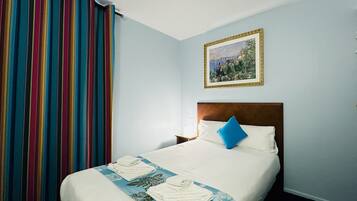 Una habitación de hotel con una cama, una colcha de diseño azul y blanco, un almohadón azul y un cuadro en la pared.
