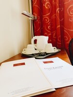 A tray with white cups and a teapot, a door with a silver handle, and a red patterned curtain.