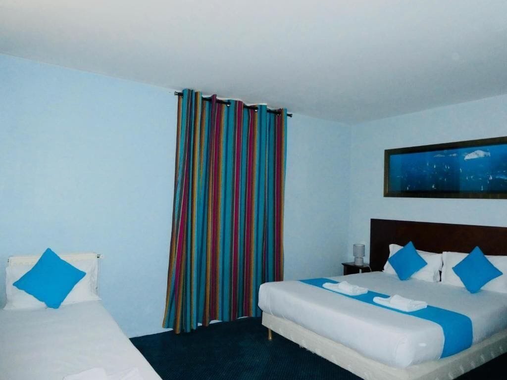 A hotel room with a bed, a smaller bed, a nightstand, a lamp, and a painting on the wall.