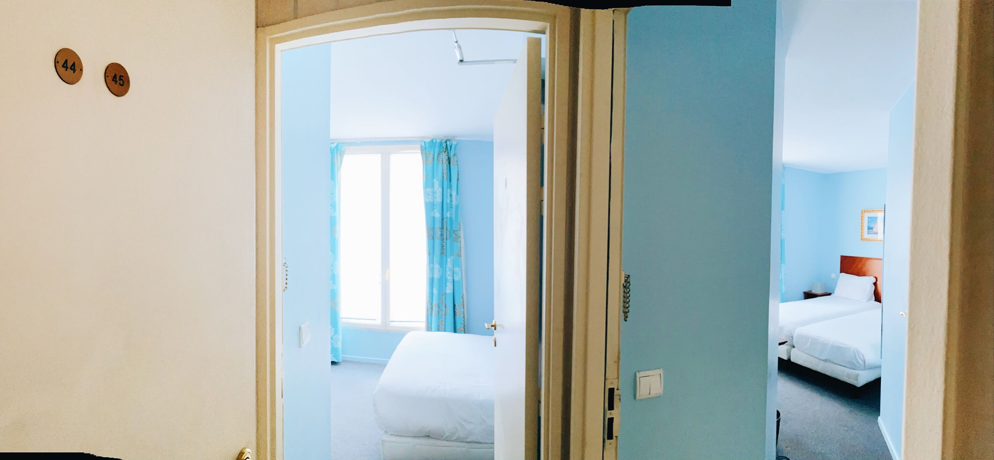 Une chambre d’hôtel avec un lit, une fenêtre avec des rideaux et une porte donnant sur une autre pièce.