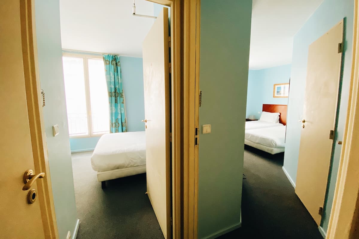 Een hotelkamer met een bed, een raam met gordijnen en een deur naar een andere kamer.