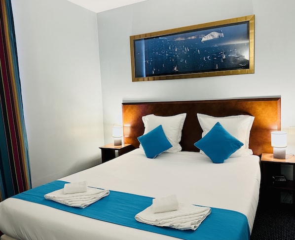 A hotel room with a large bed, two pillows, a headboard, two bedside tables with lamps, a wall-mounted painting, and a window with curtains. - Hôtel Bellevue Paris Montmartre (Paris)