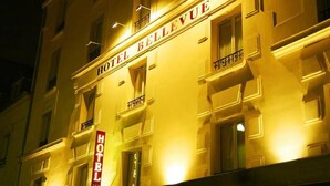 Een hotelgevel 's nachts met verlichte borden waarop 'HOTEL BELLEVUE' staat.