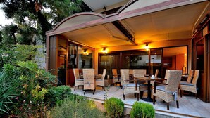 Un patio al aire libre con mobiliario de mimbre y una zona cubierta, rodeado de abundante follaje.