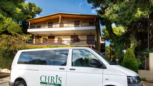 Una camioneta blanca con el rótulo 'CHRIS HOTEL' estacionada frente a un edificio con balcones.