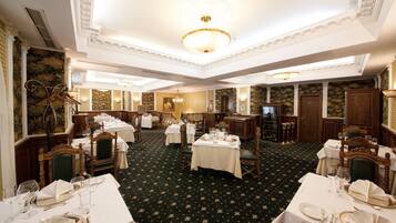 A formal dining room with multiple tables set for service, elegant chairs, and a chandelier.