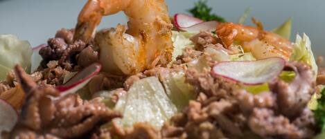A close-up of a seafood salad with shrimp, meat, and radish slices.