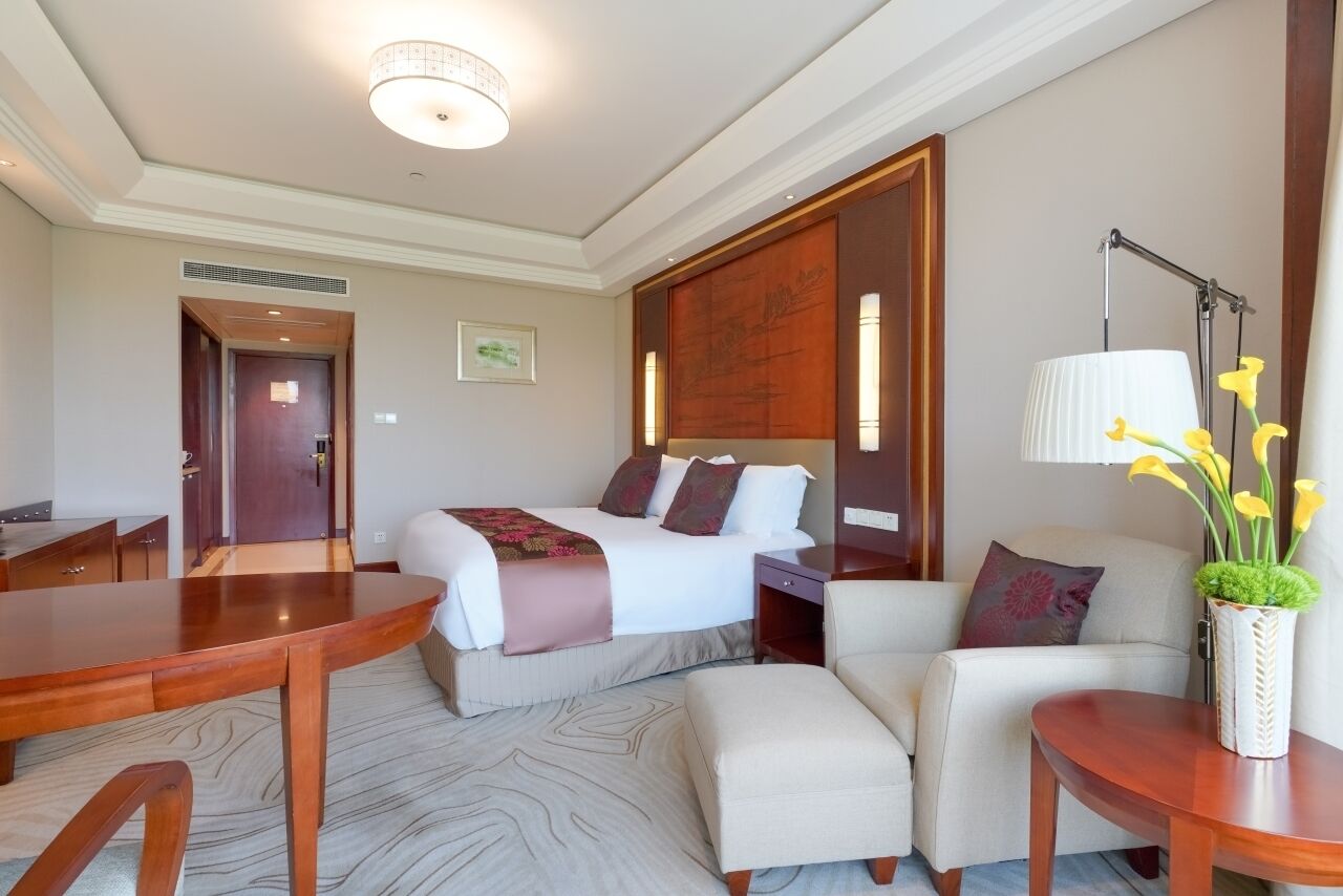 A hotel room with a bed, a sofa, a table, and a lamp.