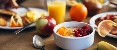 A breakfast setting with a bowl of cereal, a glass of orange juice, and various fruits on a wooden table.