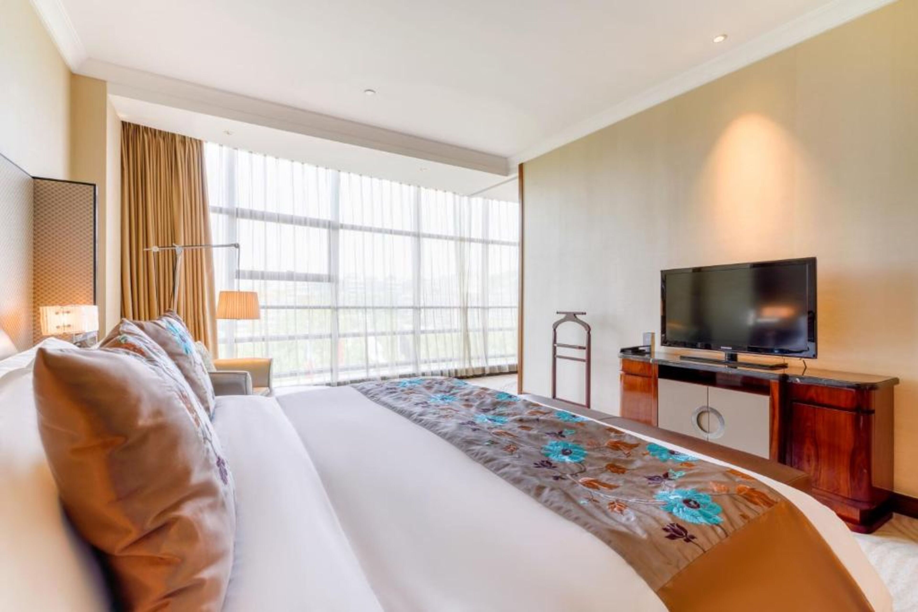 Una habitación de hotel con una cama grande, televisión, escritorio y ventana con cortinas.