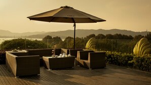 Een terras met rieten meubilair, een tafel met theepot en een grote parasol.
